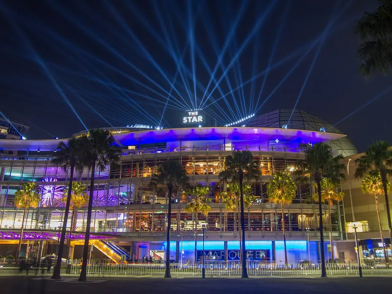 The Star casino complex in Pyrmont lit up at night with light beams above the roof and palm trees in front
